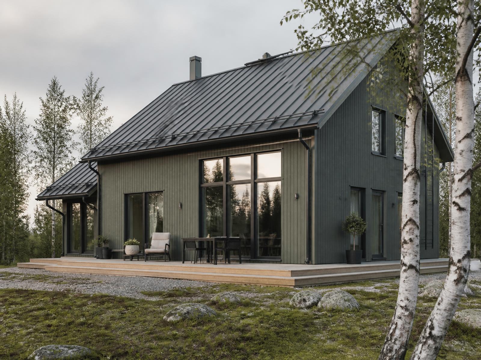 Tummanvihreä puuverhoiltu omakotitalo koivikon reunassa pilvisenä päivänä